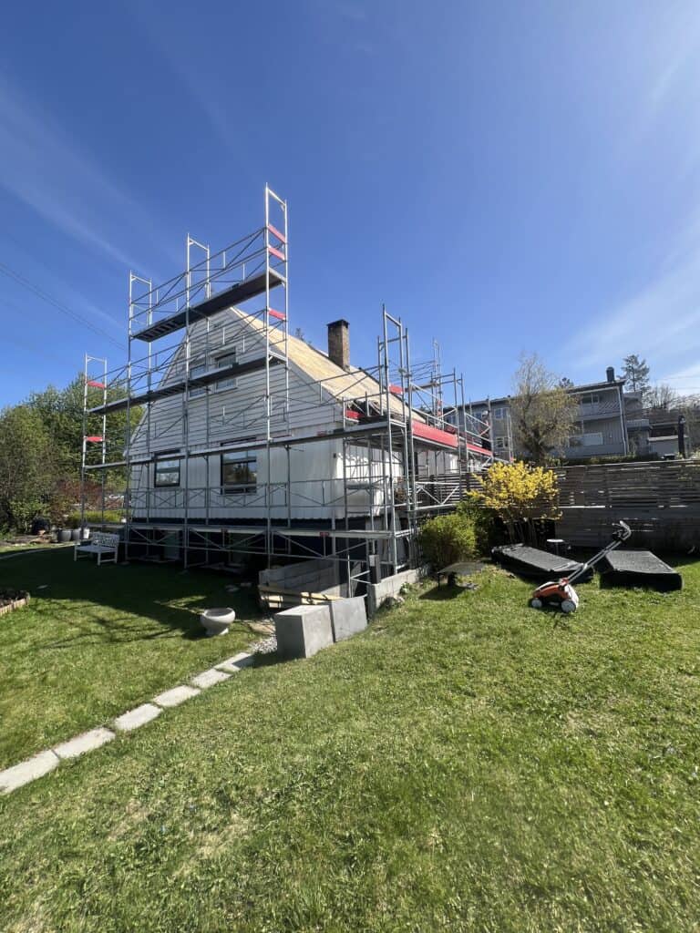 Bjarne scaffolding rundt et hvitt hus under oppussing i godt vær.