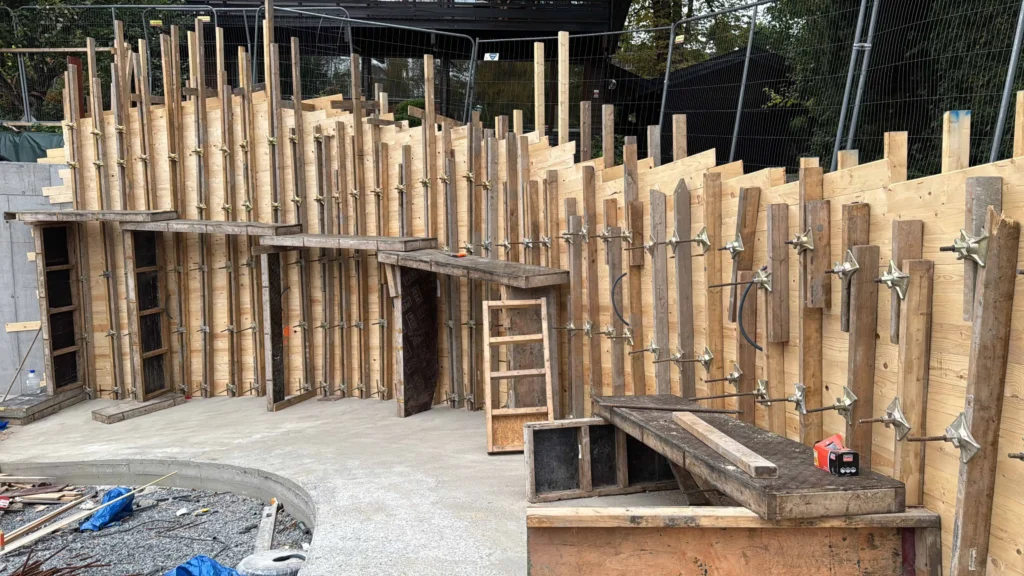 Betongsreakking foran en byggeplass med treverk og støttemurer.