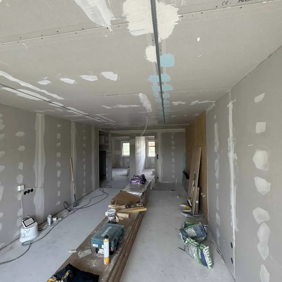 Utkantet på et nybygget rom under oppussing med dryssende gipsplater og arbeidstøy.
