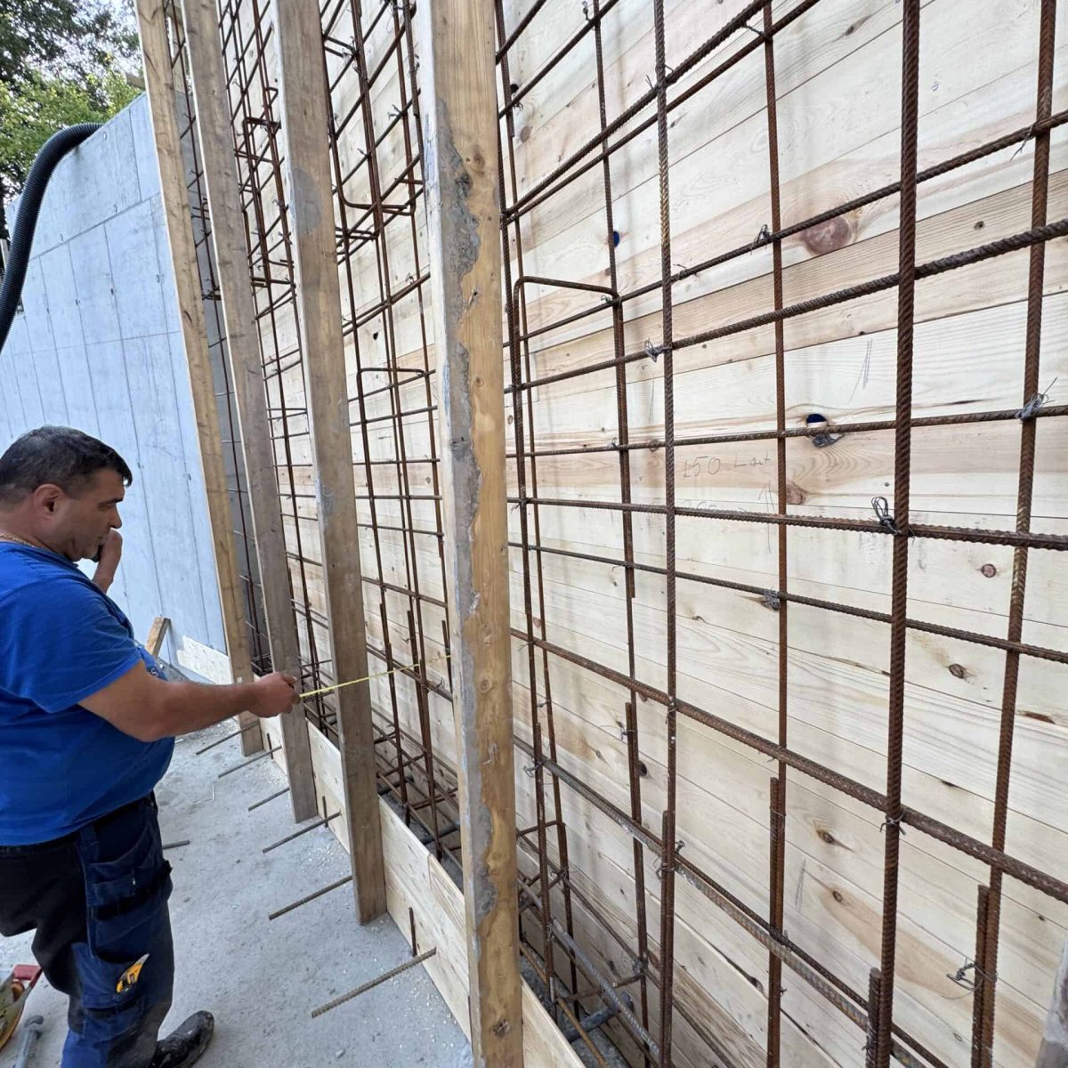 Stålarmert betongvegg under bygging med treverk og arbeidende håndverker.