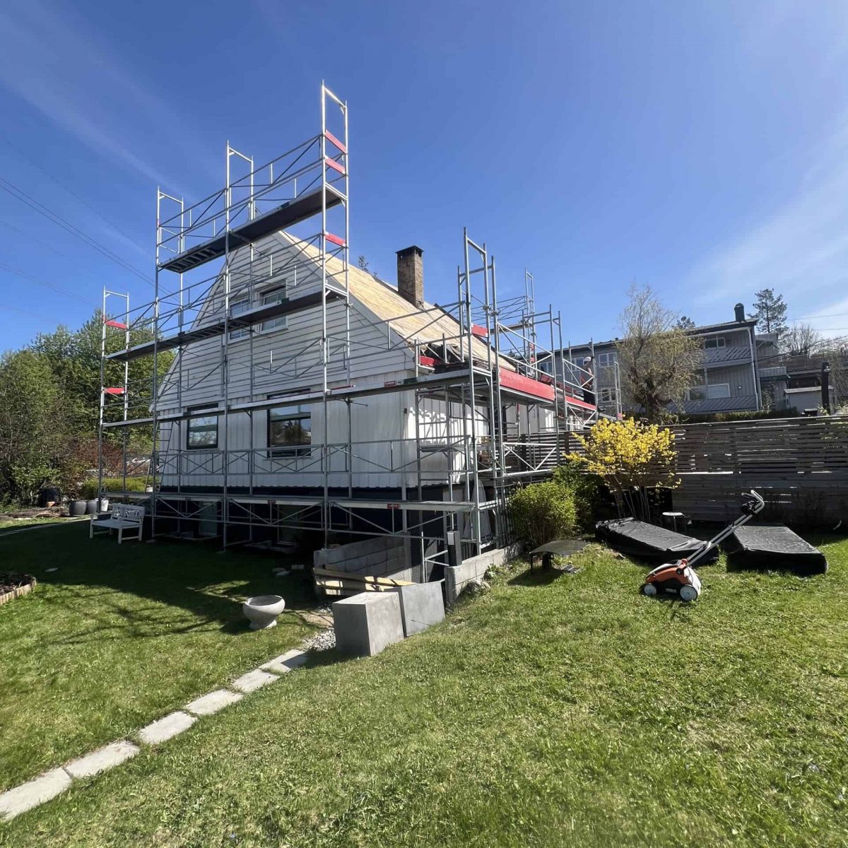 Bjarne scaffolding rundt et hvitt hus under oppussing i godt vær.