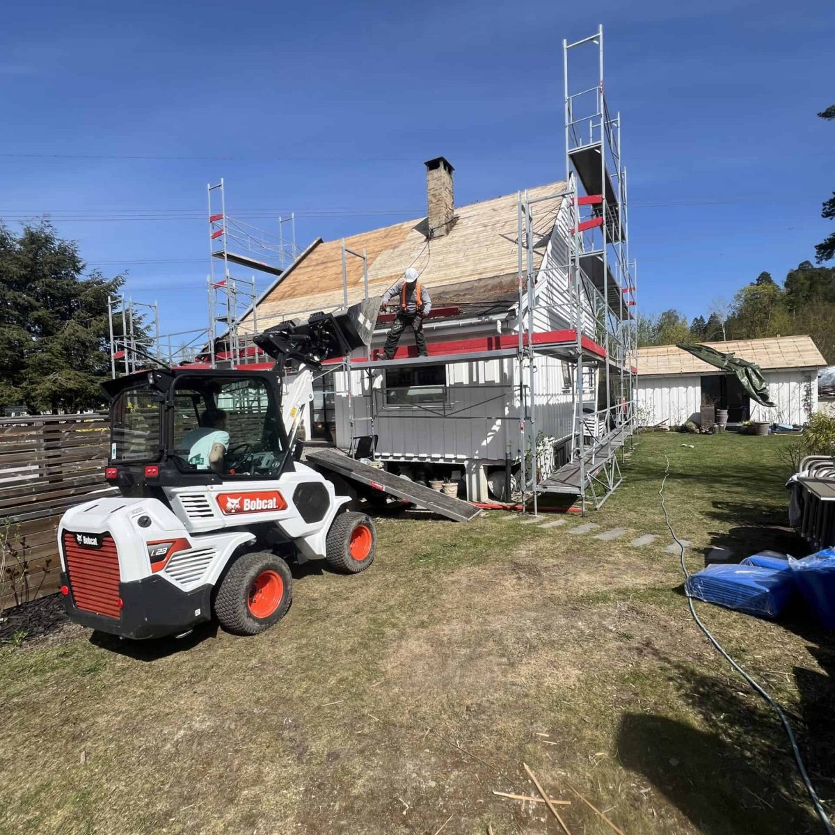 Høydearbeid på tak med byggheis og sklier, utendørs byggefirma, profesjonell taktekking, byggmester, byggarbeid.