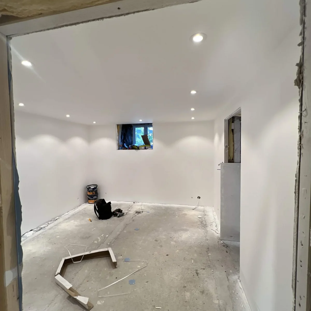 Kjernevekst av nyinnredet underetasje med hvite vegger, gulv, og innfelt takbelysning. På byggeplass under oppussing.